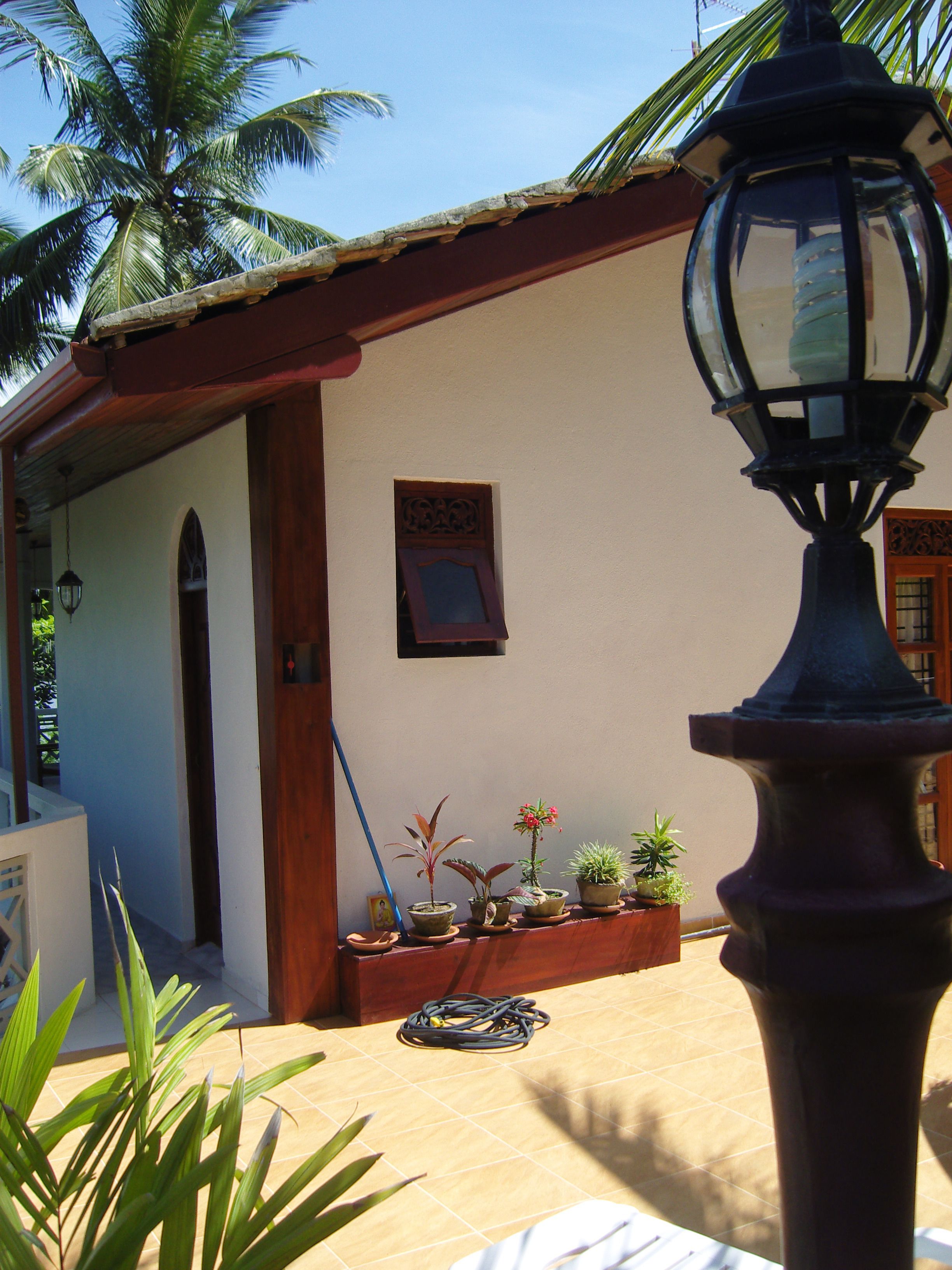 A building with a tiled patio, a wooden door, and several potted plants.