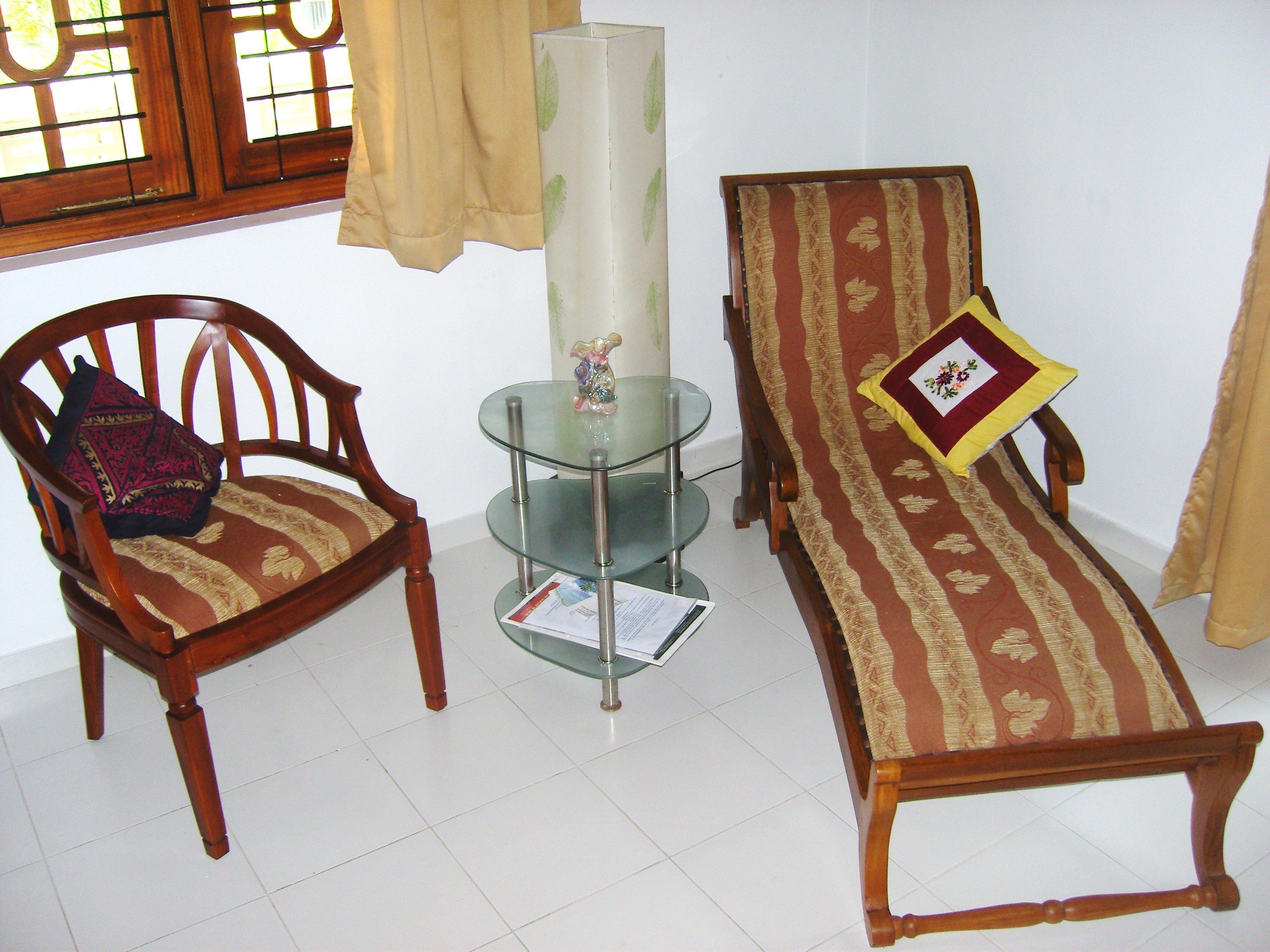 A room with a wooden chair, a glass table with a decorative item, and a sofa with a patterned cushion.