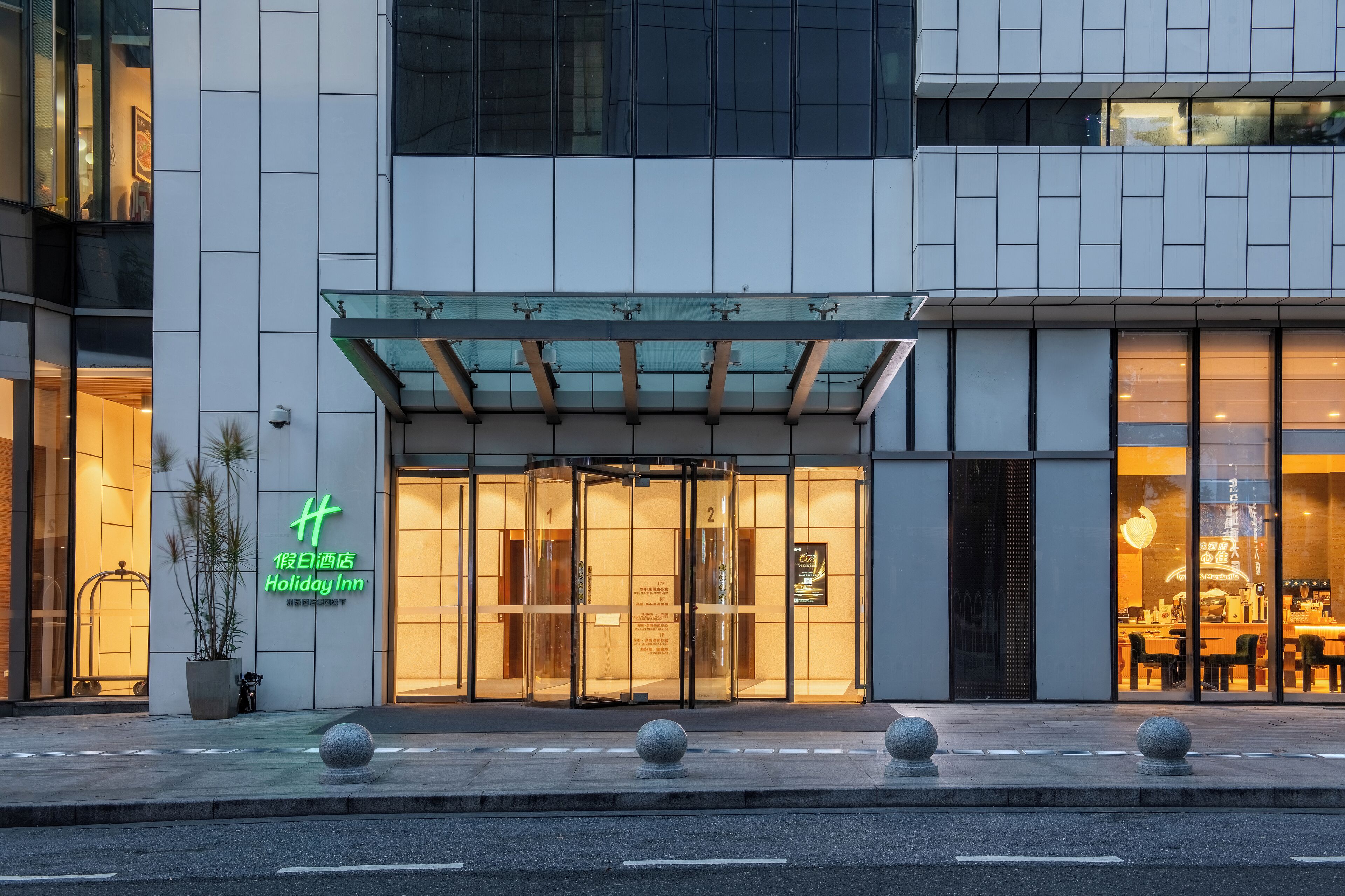 A Holiday Inn hotel entrance with a glass facade, a potted plant, and a clear view of the interior dining area.