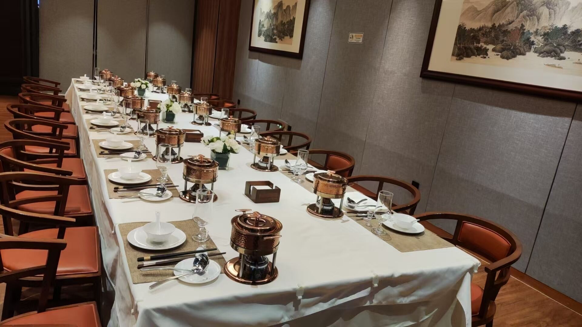 Una larga mesa de comedor dispuesta con fuentes de cobre, platos blancos y sillas de madera.