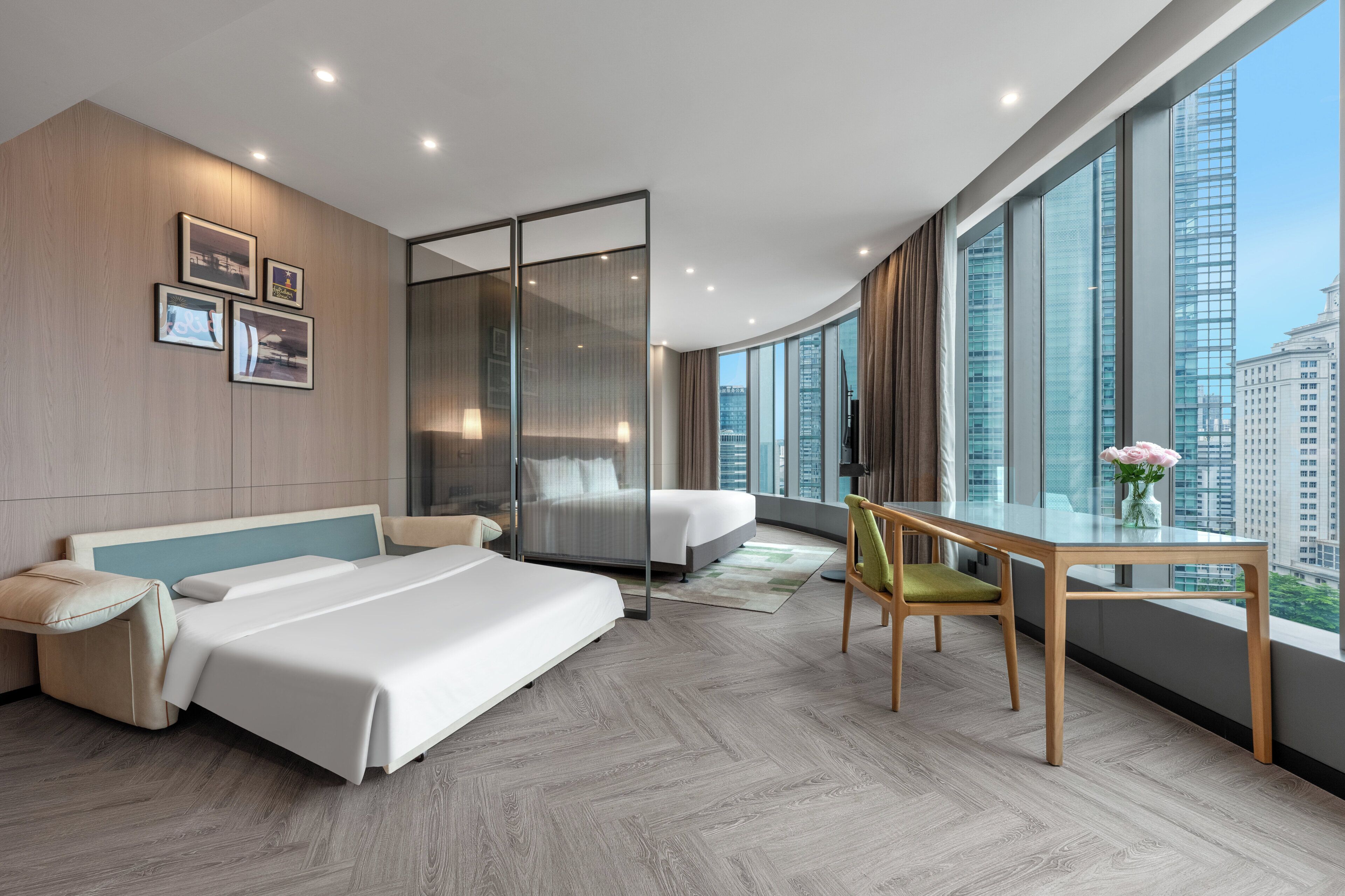 Une chambre d’hôtel moderne dotée d’un grand lit, d’un bureau avec une chaise et offrant une vue sur le paysage urbain grâce à de grandes fenêtres.