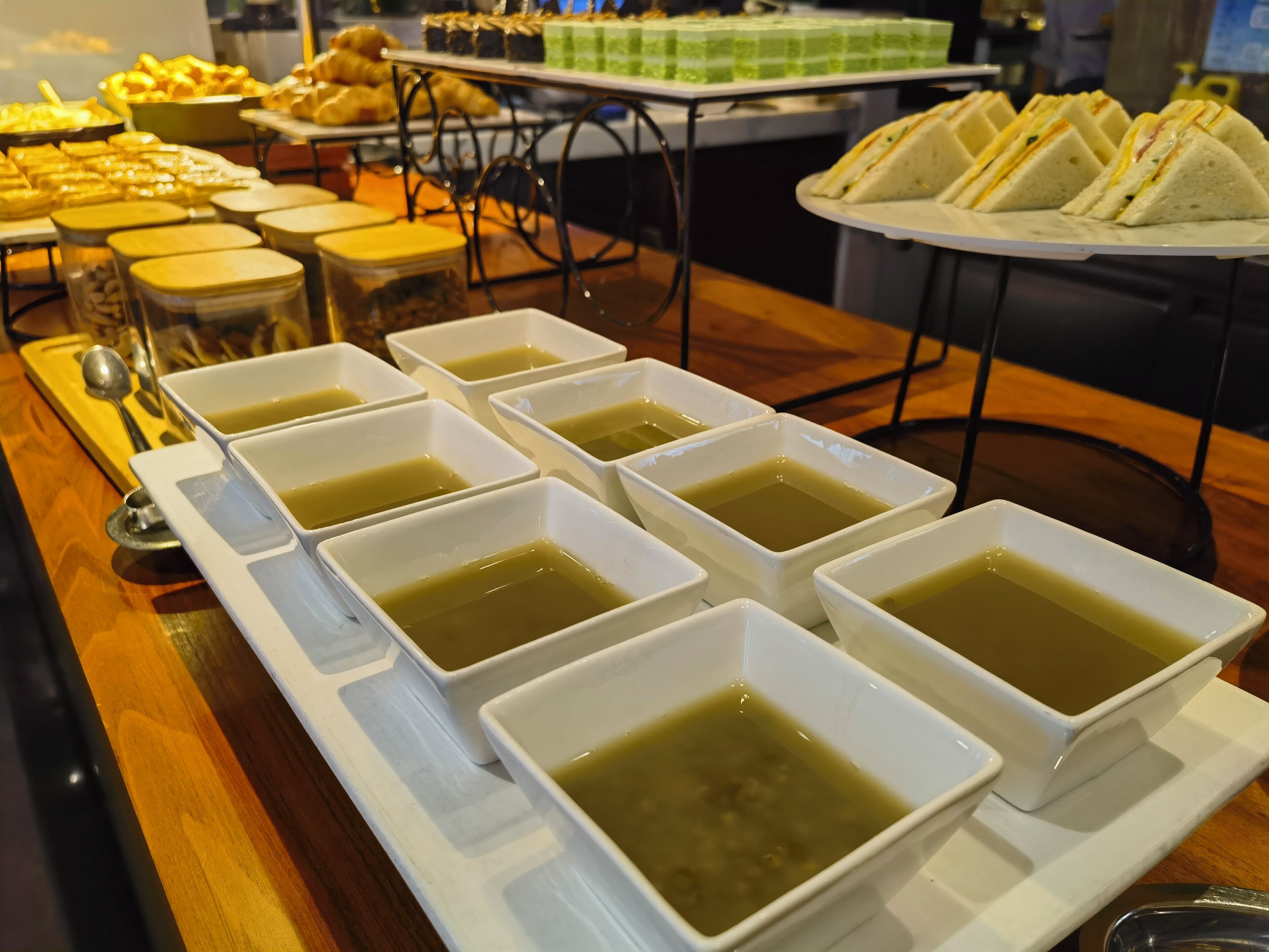 Una mesa de buffet con diversos alimentos y varias cazuelas cuadradas de sopa.