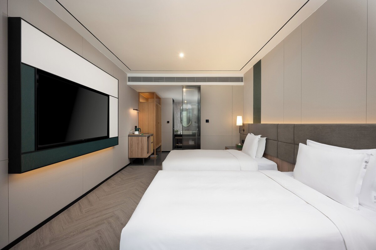 A hotel room with two beds, a TV mounted on the wall, a desk, and a wardrobe.