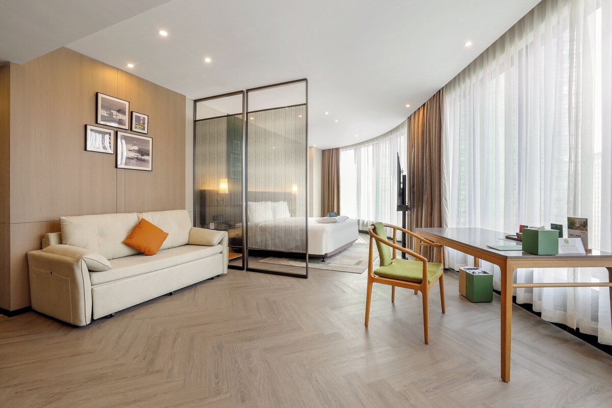 A modern hotel room with a sofa, a dining table, and a glass partition.