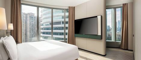 Una habitación de hotel moderna con una cama grande, un televisor de pantalla plana en la pared y grandes ventanales con vistas a la ciudad.