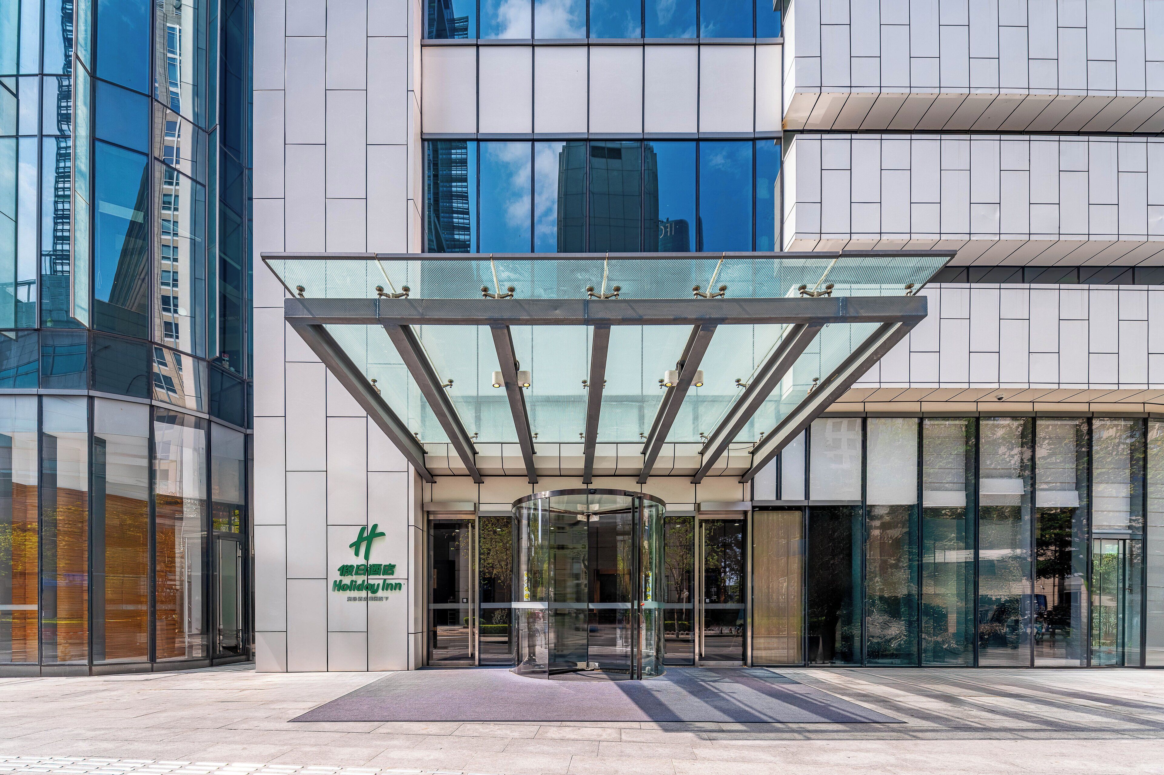 A modern hotel entrance with a revolving door, glass facade, and a clear view of the sky.