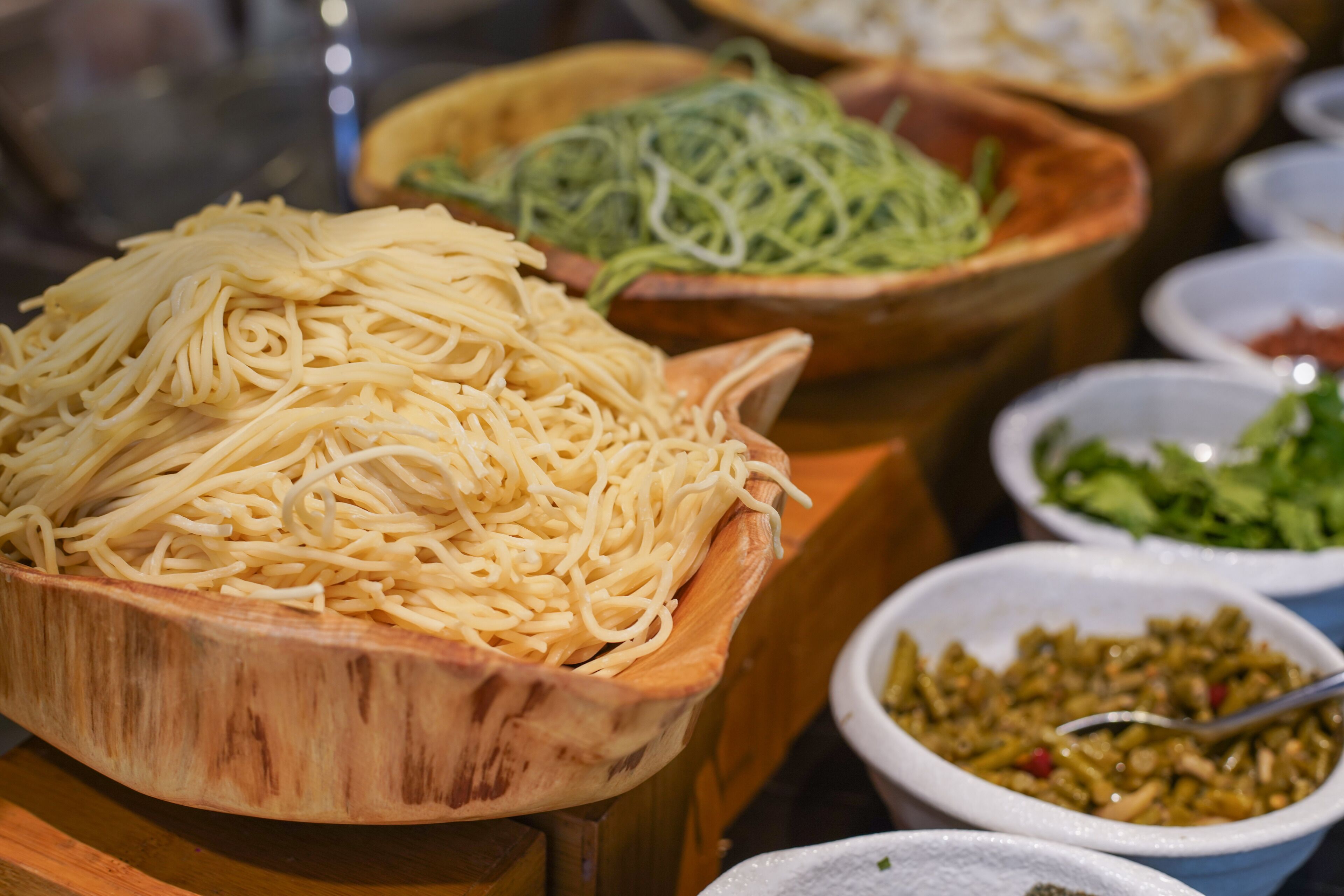 A variety of food items displayed in wooden bowls, including noodles, shredded vegetables, and a salad.