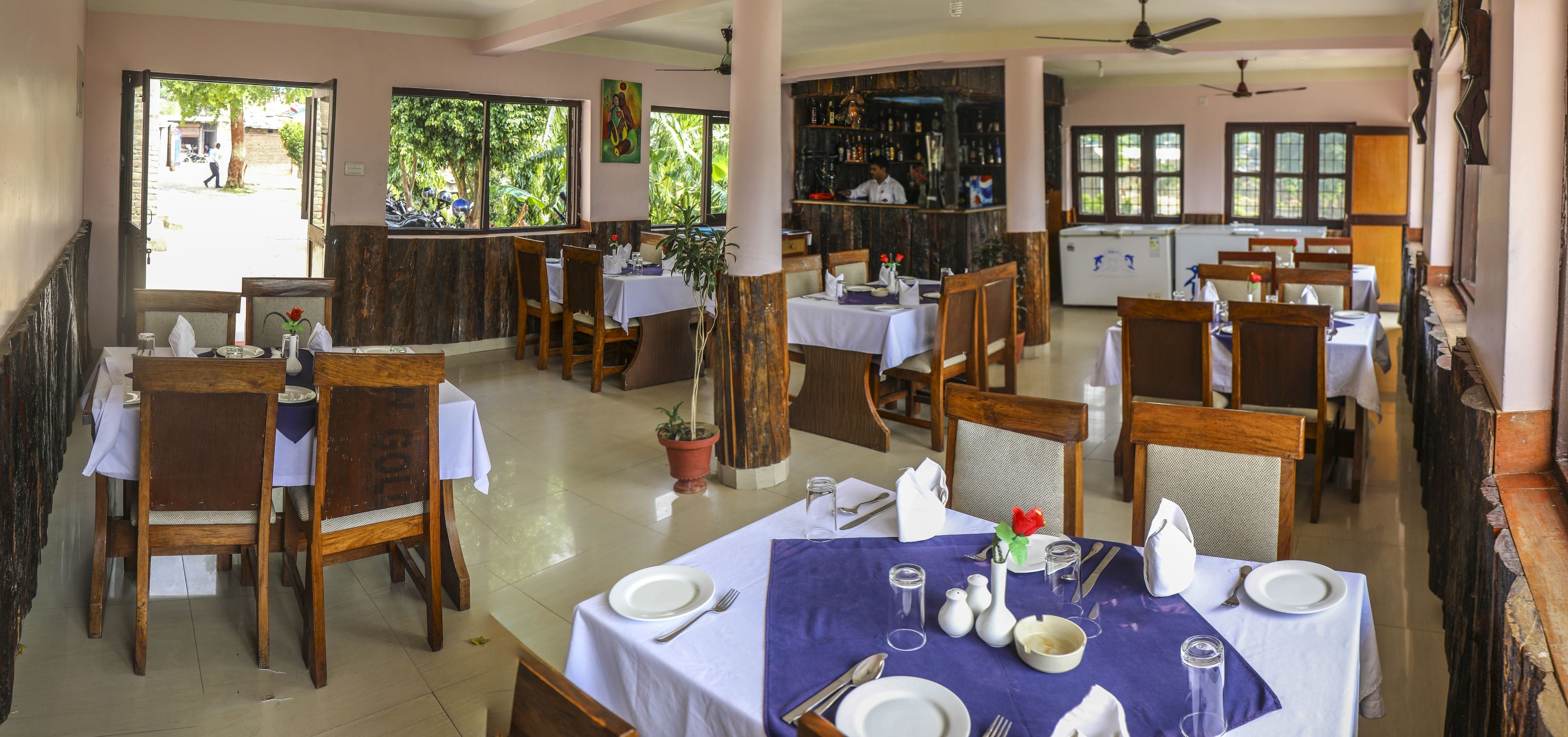 Un restaurant amb diverses taules preparades per dinar, una zona de bar i vista cap a l'exterior.