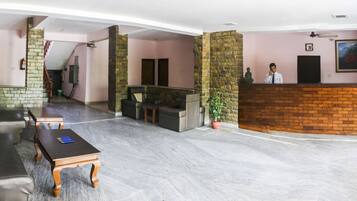 A hotel lobby with a reception desk, seating area, and a staircase leading to an upper floor.