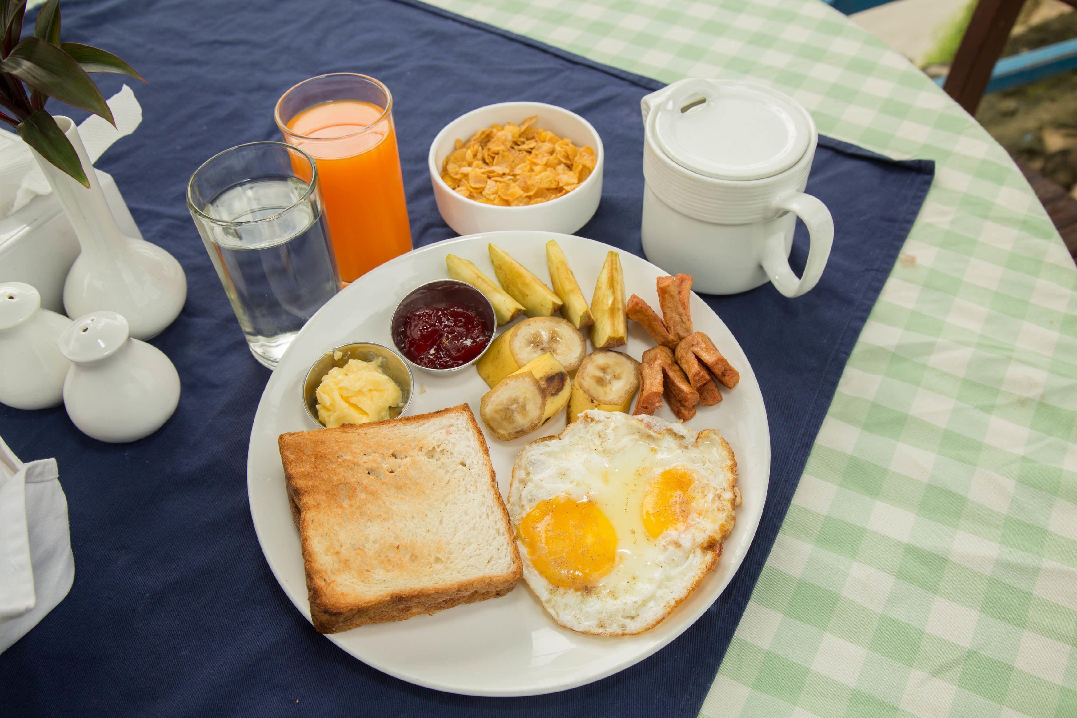 A breakfast plate with toast, eggs, bananas, and fries on a checkered tablecloth.