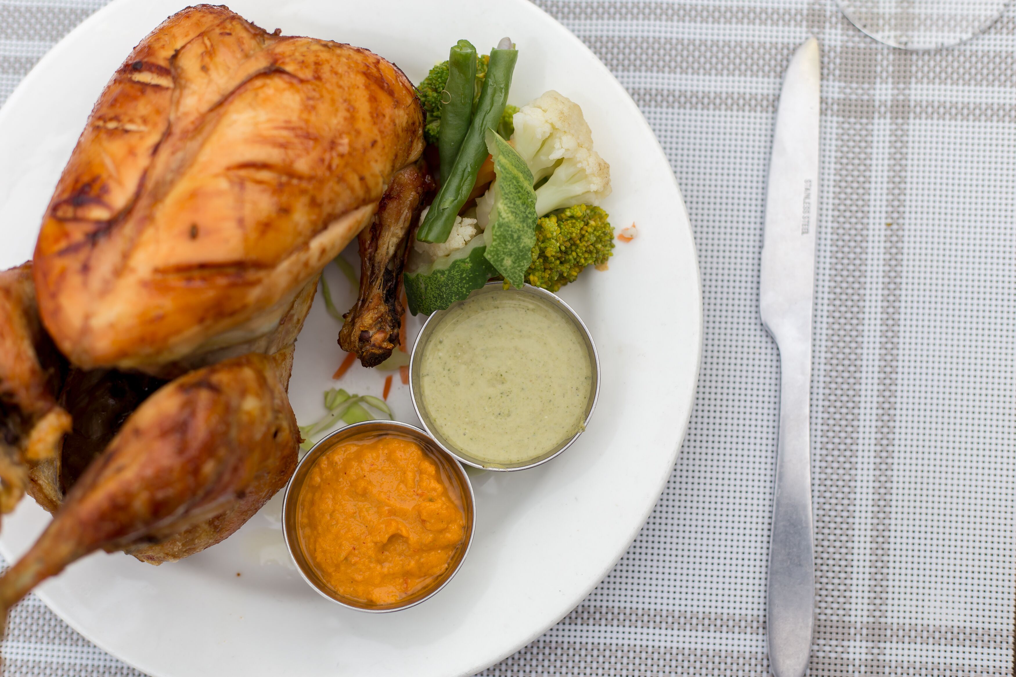 A plate with roasted chicken, green beans, cauliflower, and two dipping sauces.