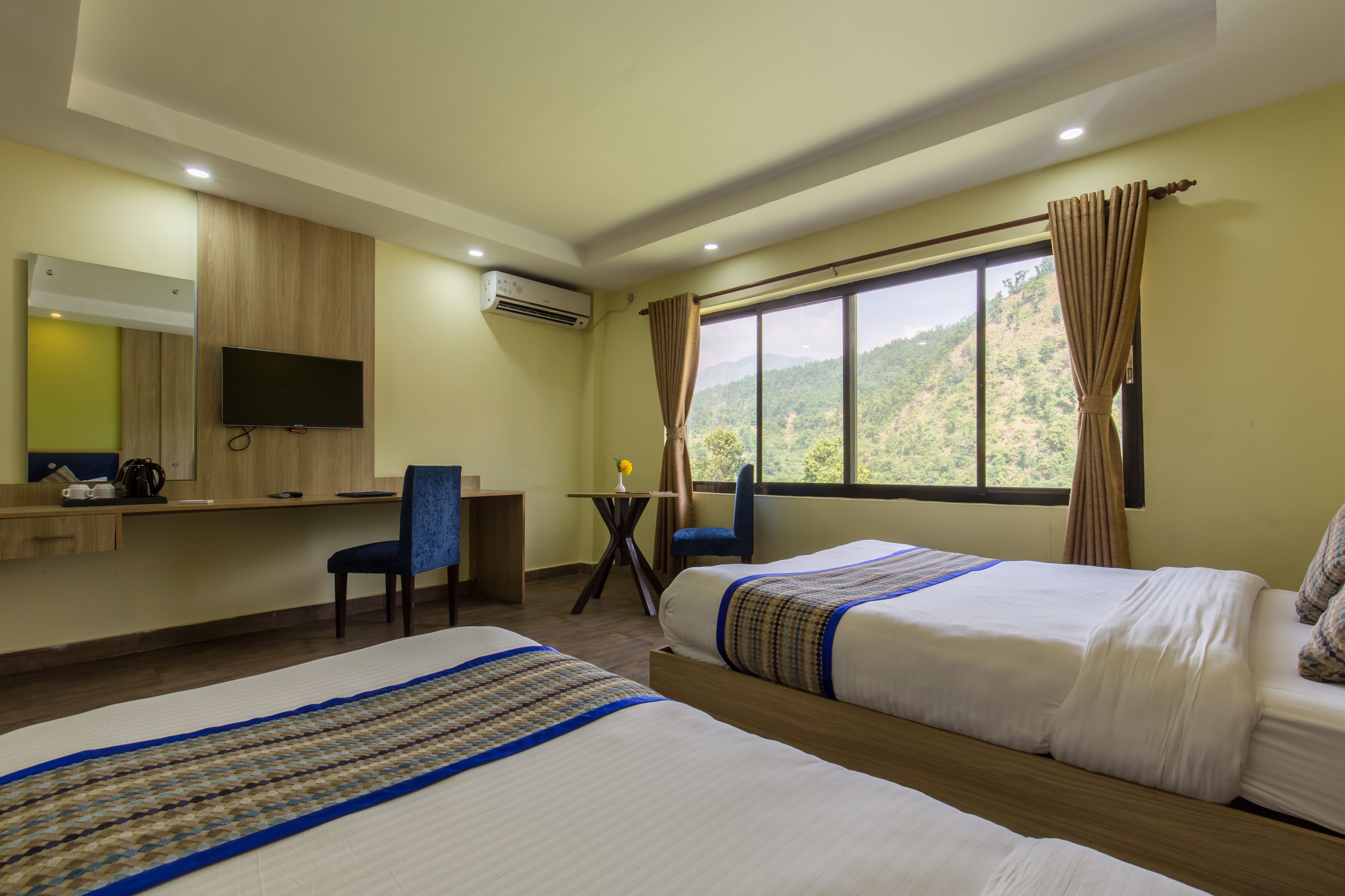 A hotel room with two beds, a desk, a chair, a TV, and a window with curtains.