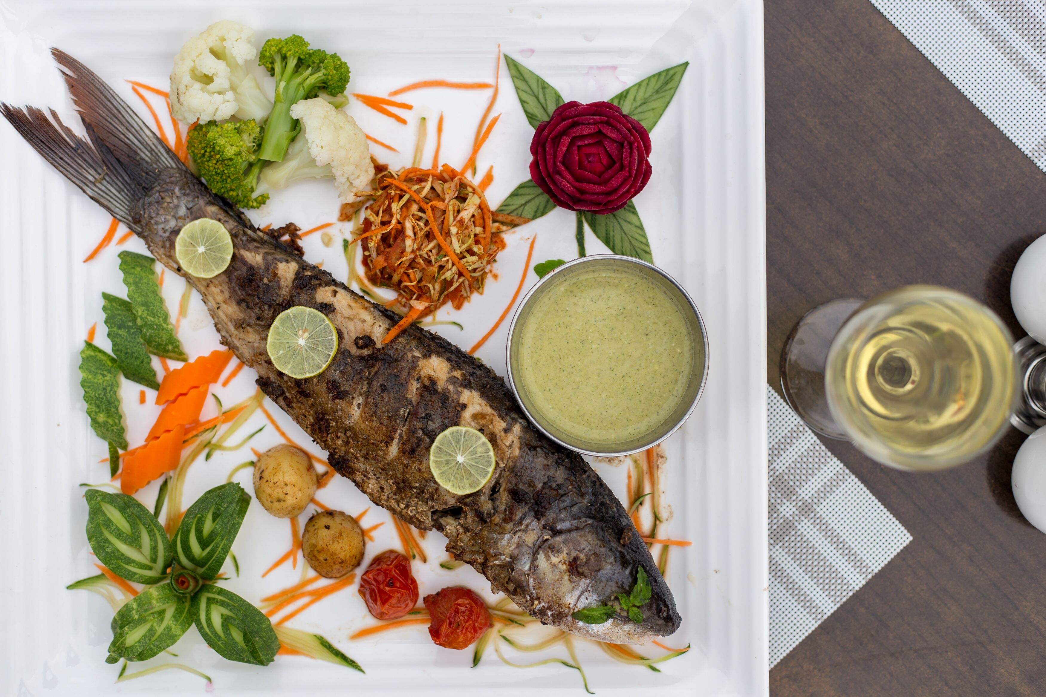 Un plato con un pescado entero, verduras y salsa.