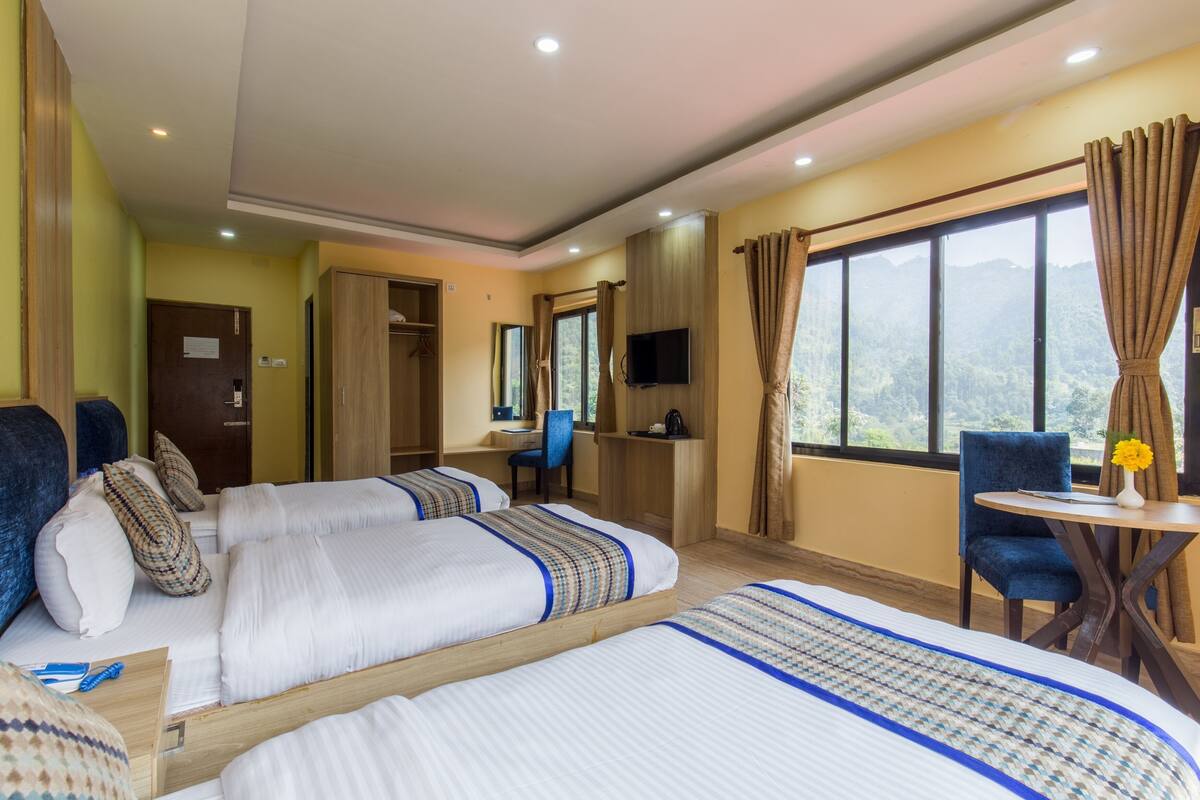 Habitación de hotel con dos camas, un escritorio, una silla, un televisor y una ventana con vista a la montaña.