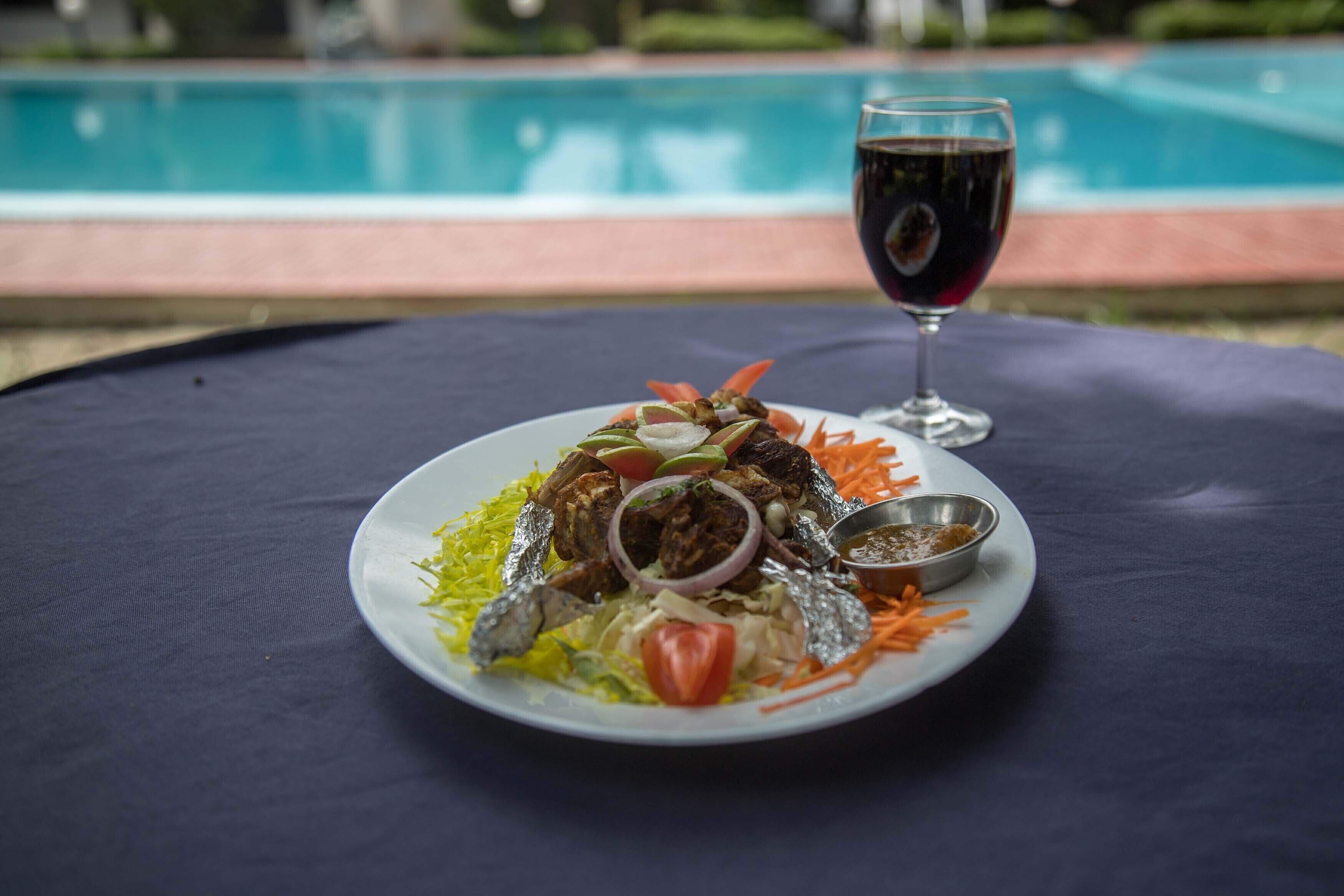 Une assiette de nourriture et un verre de vin rouge, posés sur une table près d’une piscine.