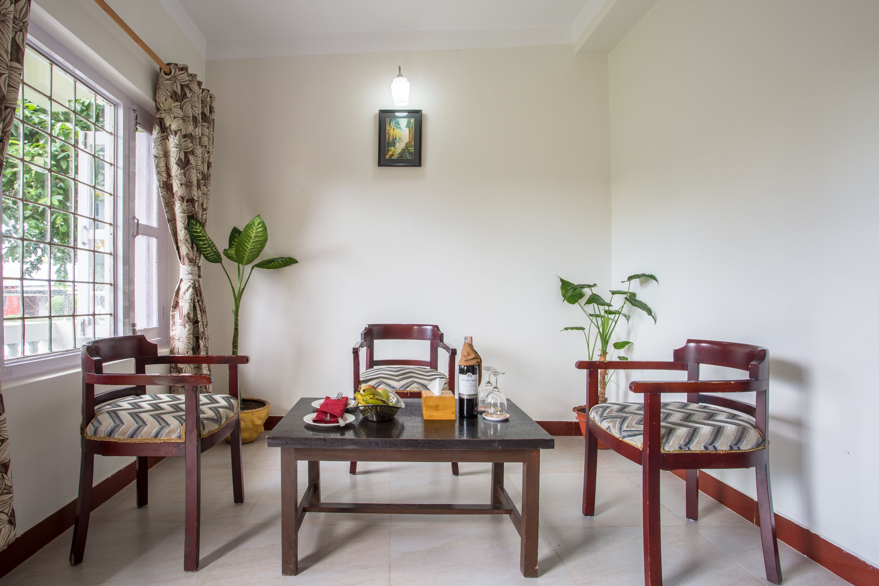 Un comedor con una mesa y cuatro sillas, una planta en maceta, un cuadro en la pared y una ventana con cortinas.
