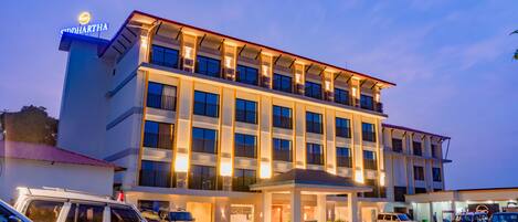 A multi-story hotel with a prominent sign, multiple balconies, and a parking area with several vehicles.