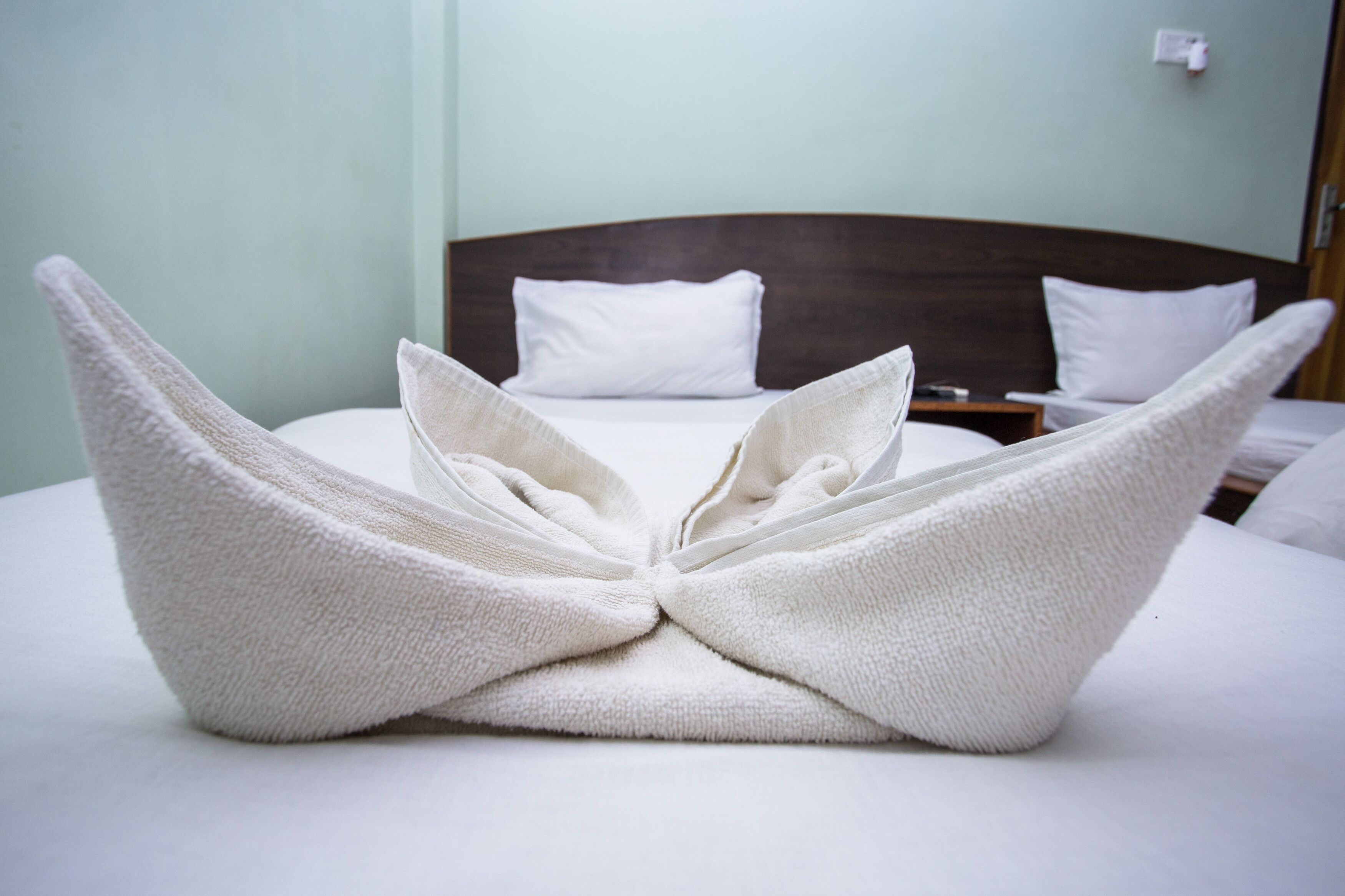 A neatly made bed with white linens and pillows, a wooden headboard, and a bedside table with a lamp.