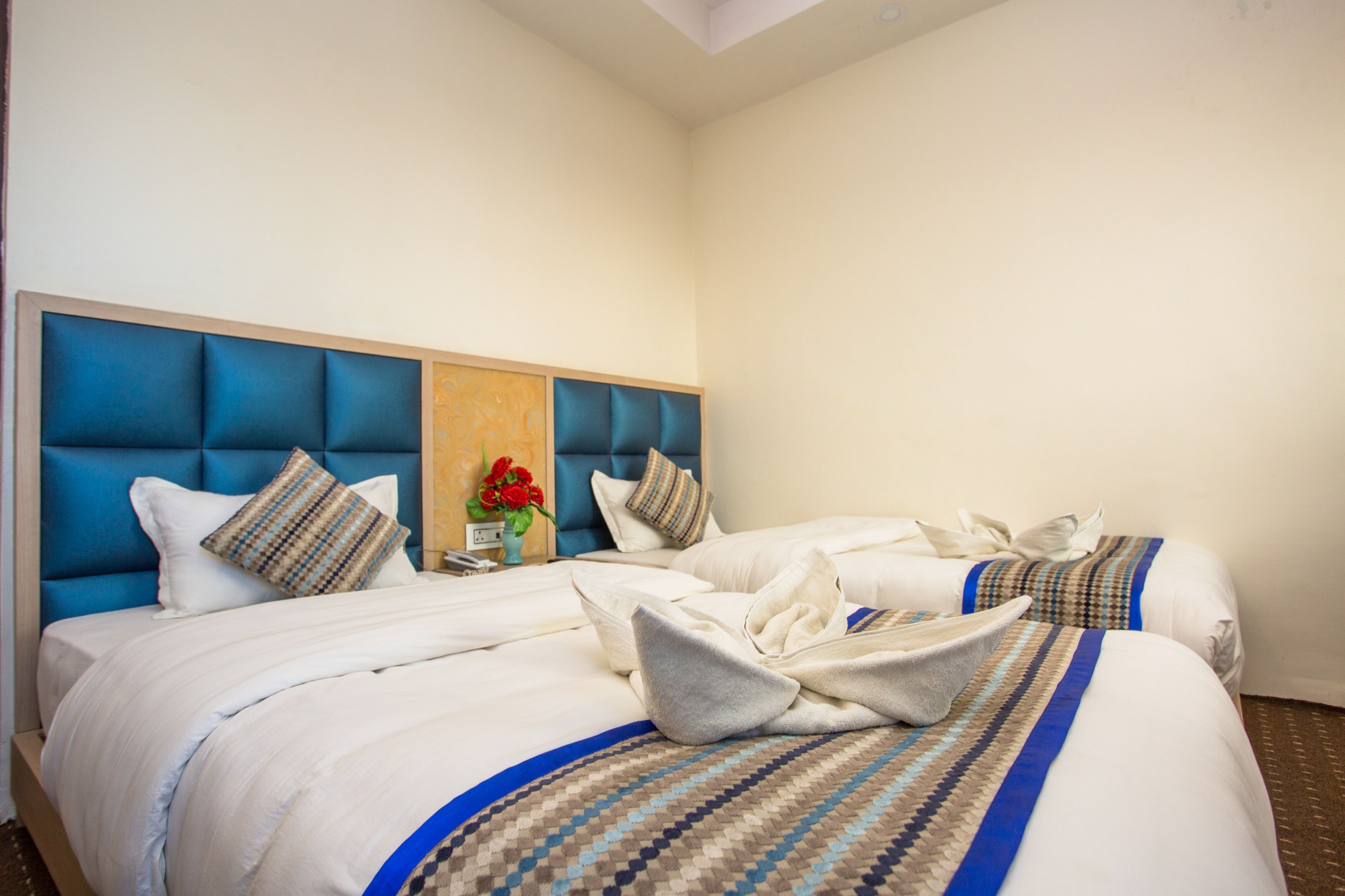 Una habitación de hotel con dos camas, un cabecero azul y un florero con flores rojas.