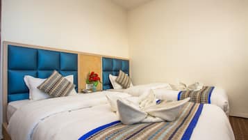 A hotel room with two beds, a blue headboard, and a vase with red flowers.