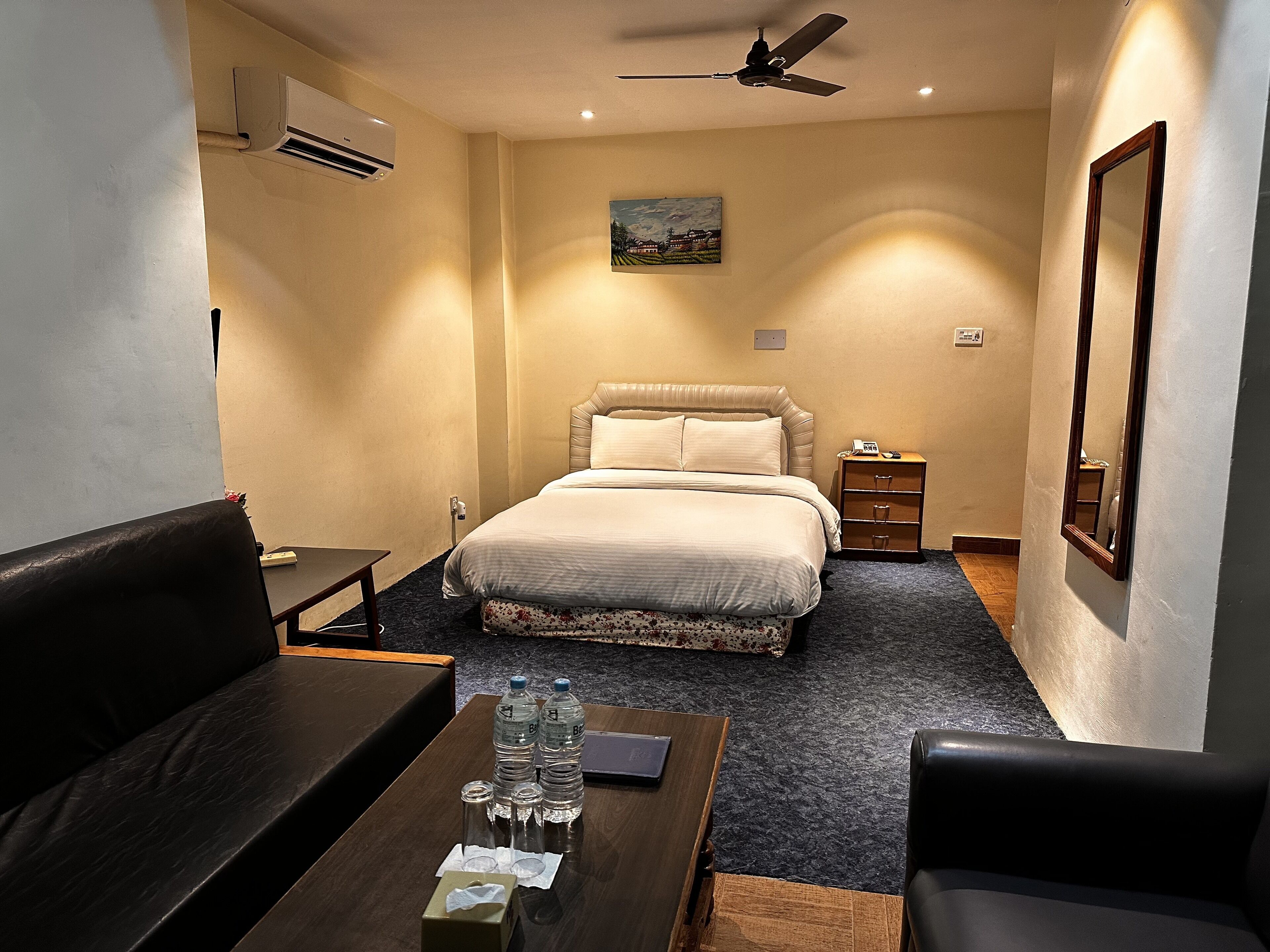 A hotel room with a bed, a sofa, a coffee table, a nightstand, and a ceiling fan.