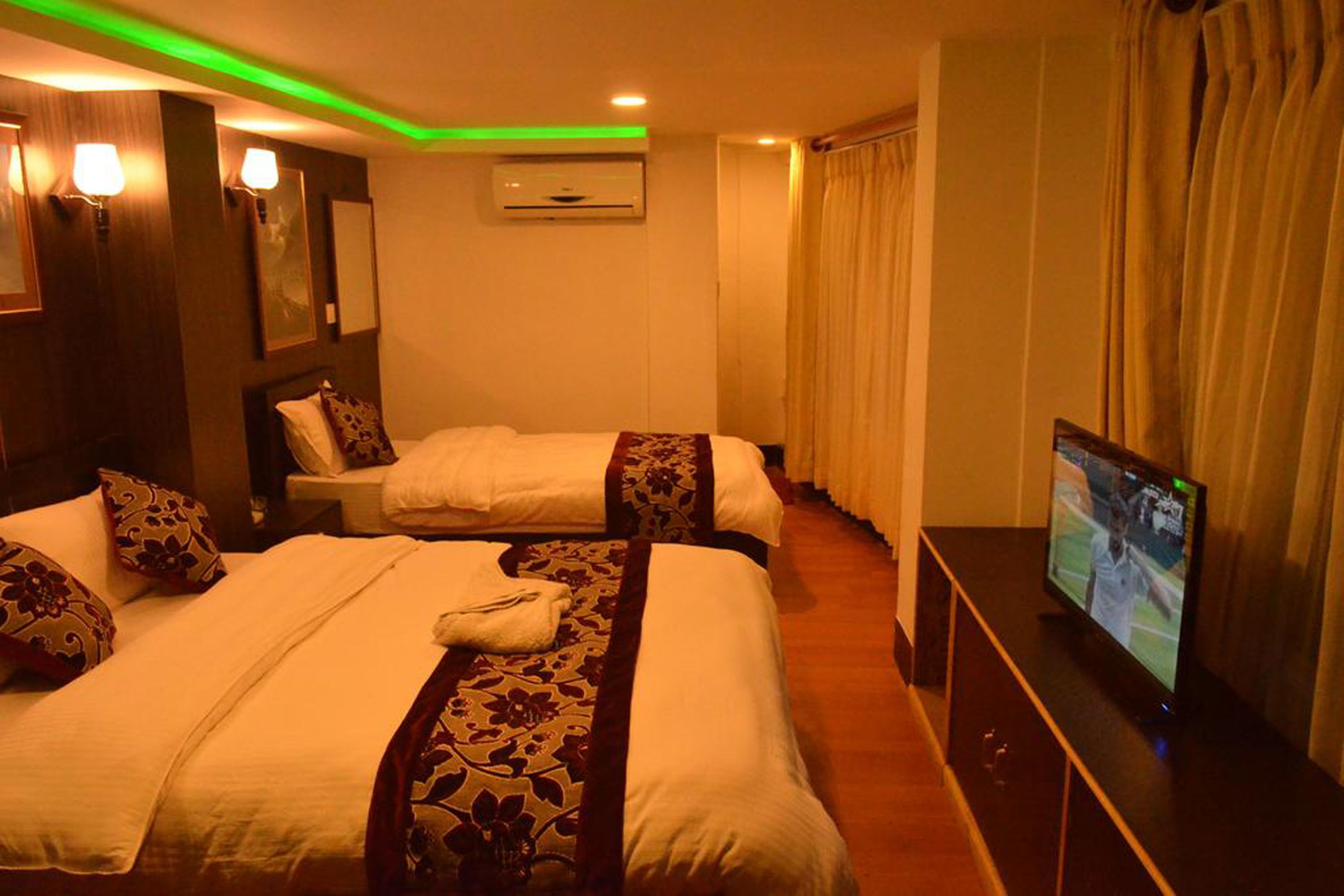 A hotel room with two beds, a television, and a wall-mounted air conditioner.