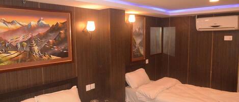 Habitación de hotel con dos camas, paneles de madera, aire acondicionado instalado en la pared y un cuadro grande con un paisaje montañoso.