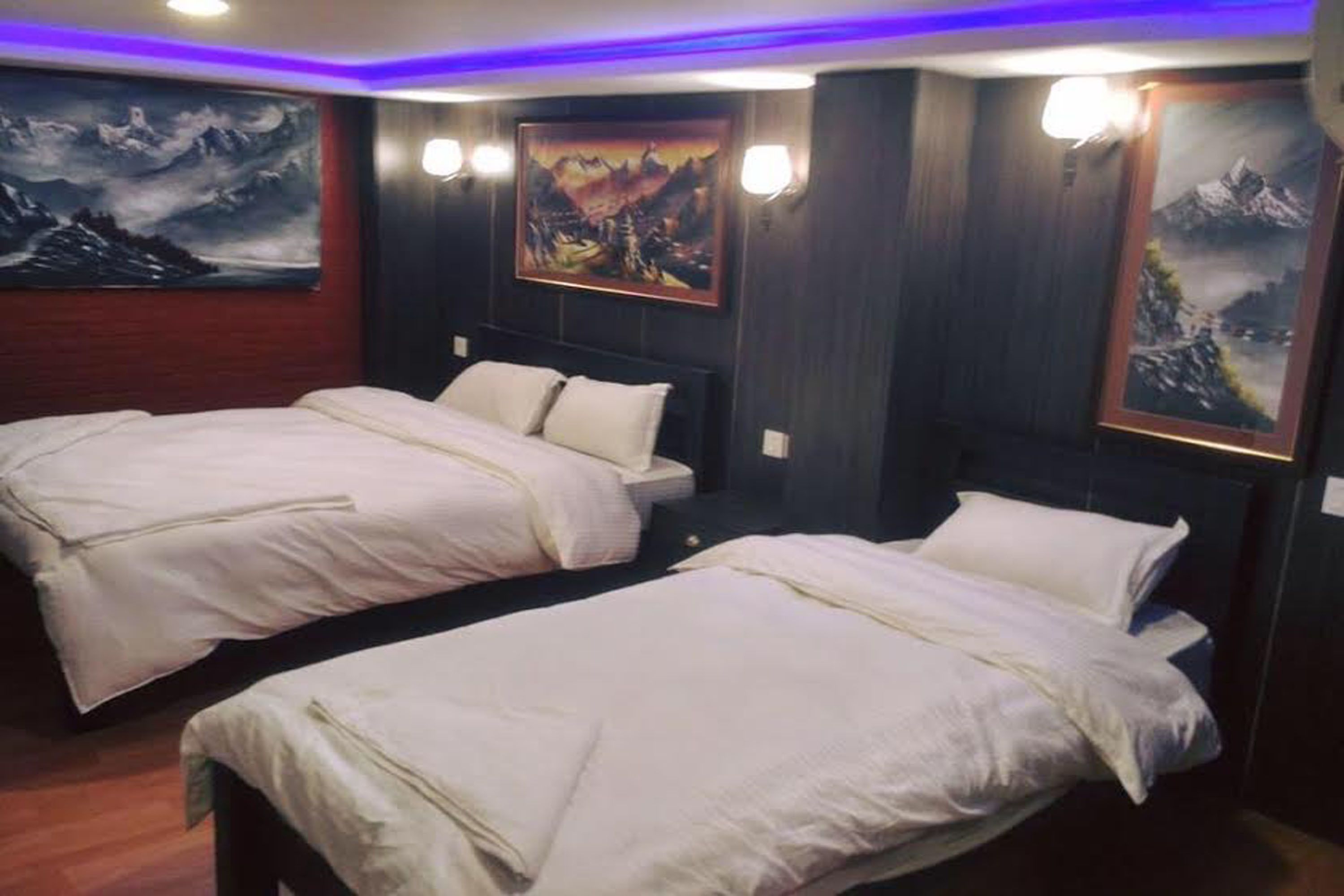 A hotel room with two beds, wooden paneling, and mountain-themed artwork on the walls.