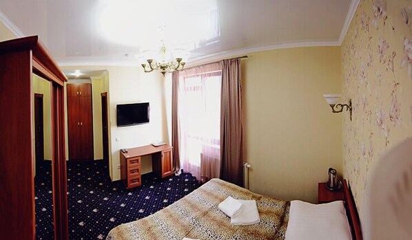 A hotel room with a bed, a desk, a television, and a chandelier. - Afrodita Hotel (Truskavets)