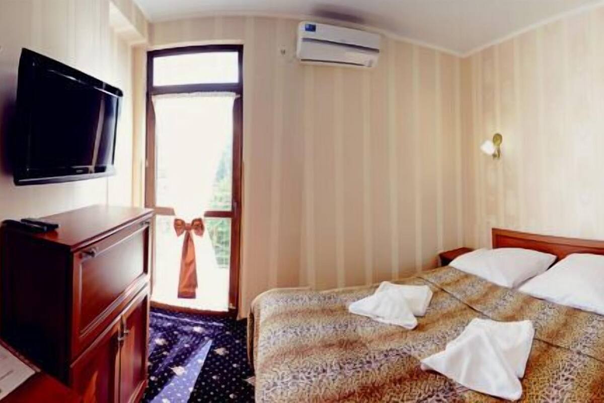 Una habitación de hotel con cama, televisión, cómoda, espejo y ventana.