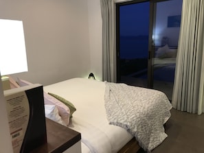 Ein Hotelzimmer mit Bett, Nachttisch mit Lampe, einem Fenster mit Vorhängen und Blick nach draußen.