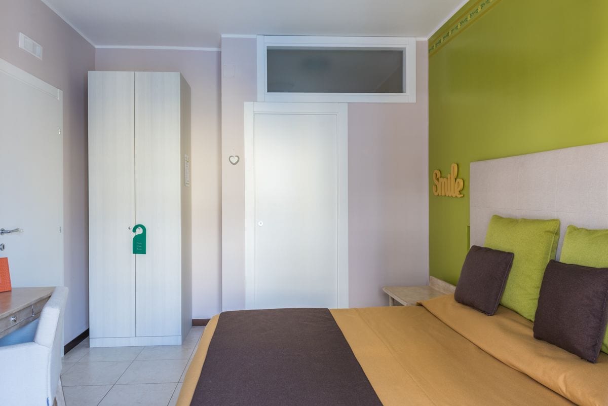 A bedroom with a bed, a wardrobe, a desk, and a green wall with a 'Smile' sign.