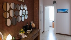 A reception area with a 'Welcome' sign, multiple mirrors, a wooden desk with bottles and a vase of flowers, and a hallway leading to a room with a painting. - KiBari B&B (Bari)