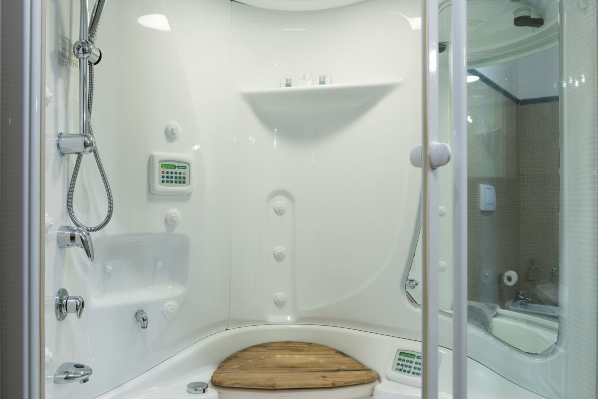 Une salle de bain moderne dotée d’une paroi de douche en verre, d’un abattant de toilettes en bois, d’un lavabo encastré et d’une douchette à main.