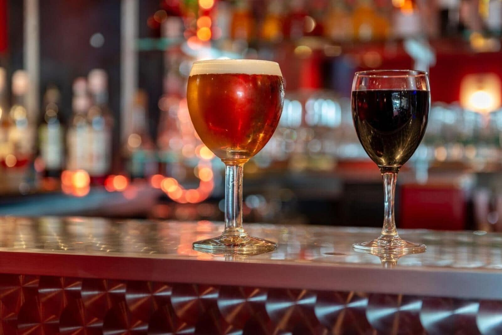 Dos vasos de bebidas sobre una barra, con un fondo borroso de botellas y luces.