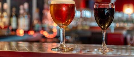 Two glasses of beverages on a bar counter with a blurred background of bottles and lights.