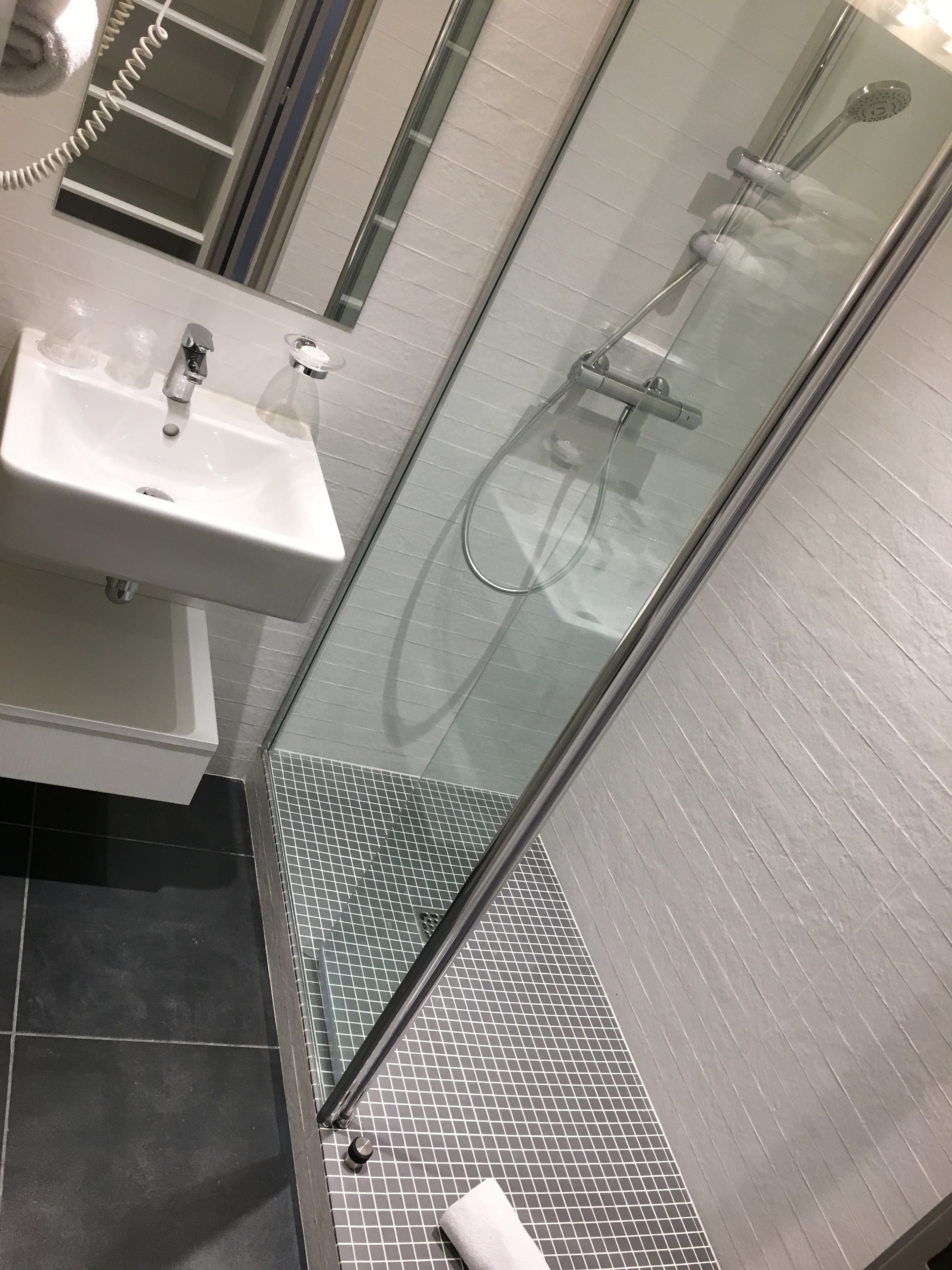 A modern bathroom with a glass-enclosed shower, a white sink, and a tiled floor.