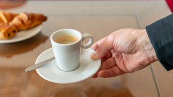 Une main tenant une tasse blanche avec une cuillère posée sur une soucoupe, le tout placé sur une table en bois.