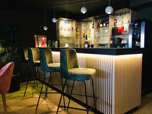 Zona de bar con mostrador, taburetes y estantes llenos de botellas y vasos.