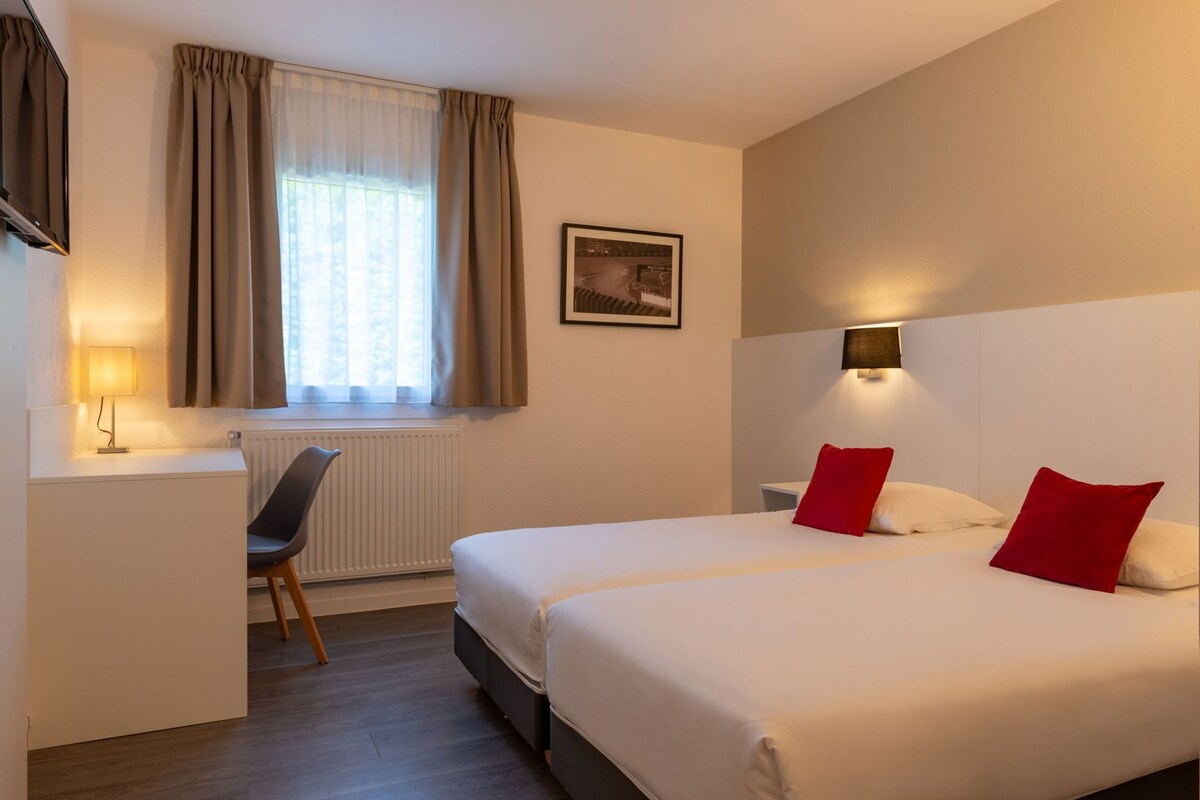 Een hotelkamer met een bed, een bureau, een stoel, een radiator en een raam met gordijnen.
