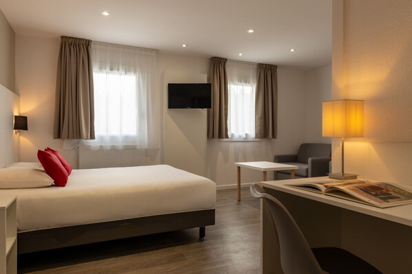 Una habitación de hotel moderna con cama, escritorio, silla, televisión y dos ventanas con cortinas.