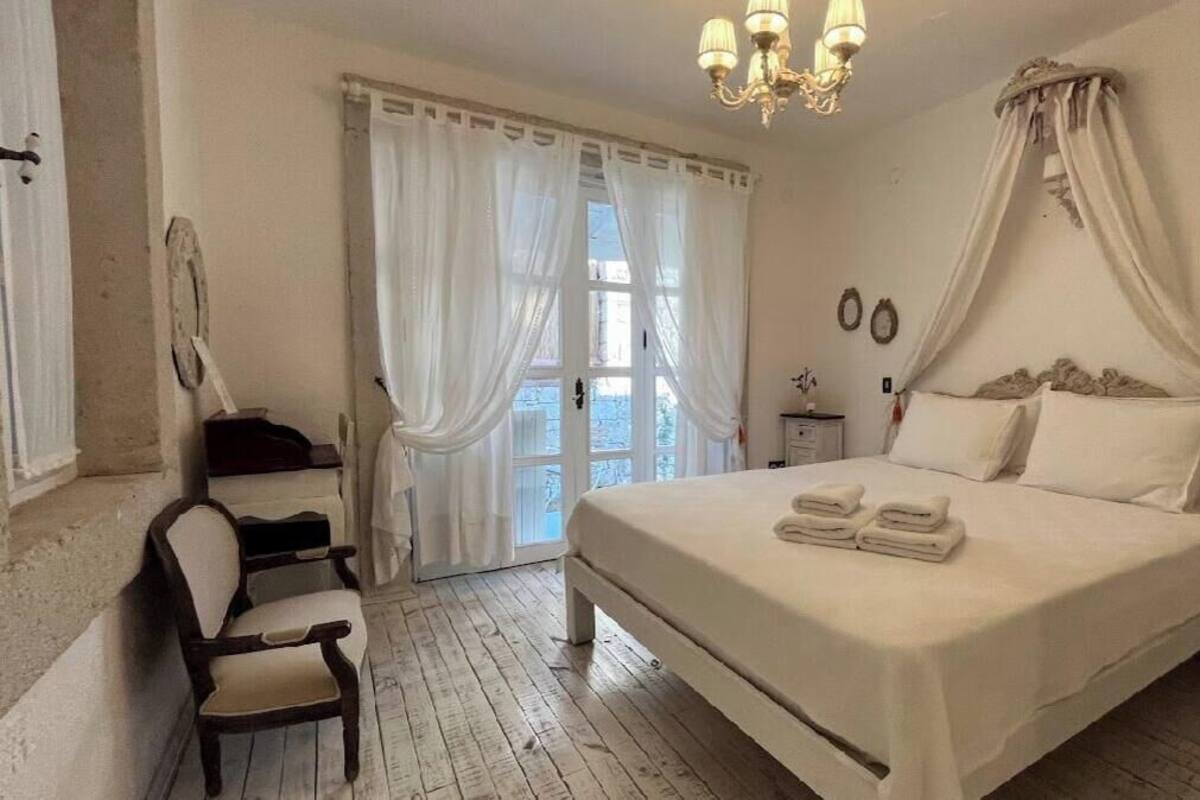 A bedroom with a large bed, a chair, a desk, and a window with curtains.