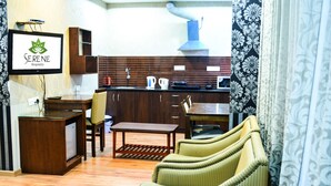 Ein Hotelzimmer mit Holzboden, einer Couch, einem kleinen Tisch, einer Küchenzeile mit Herd und Spüle sowie einem an der Wand befestigten Fernseher.
