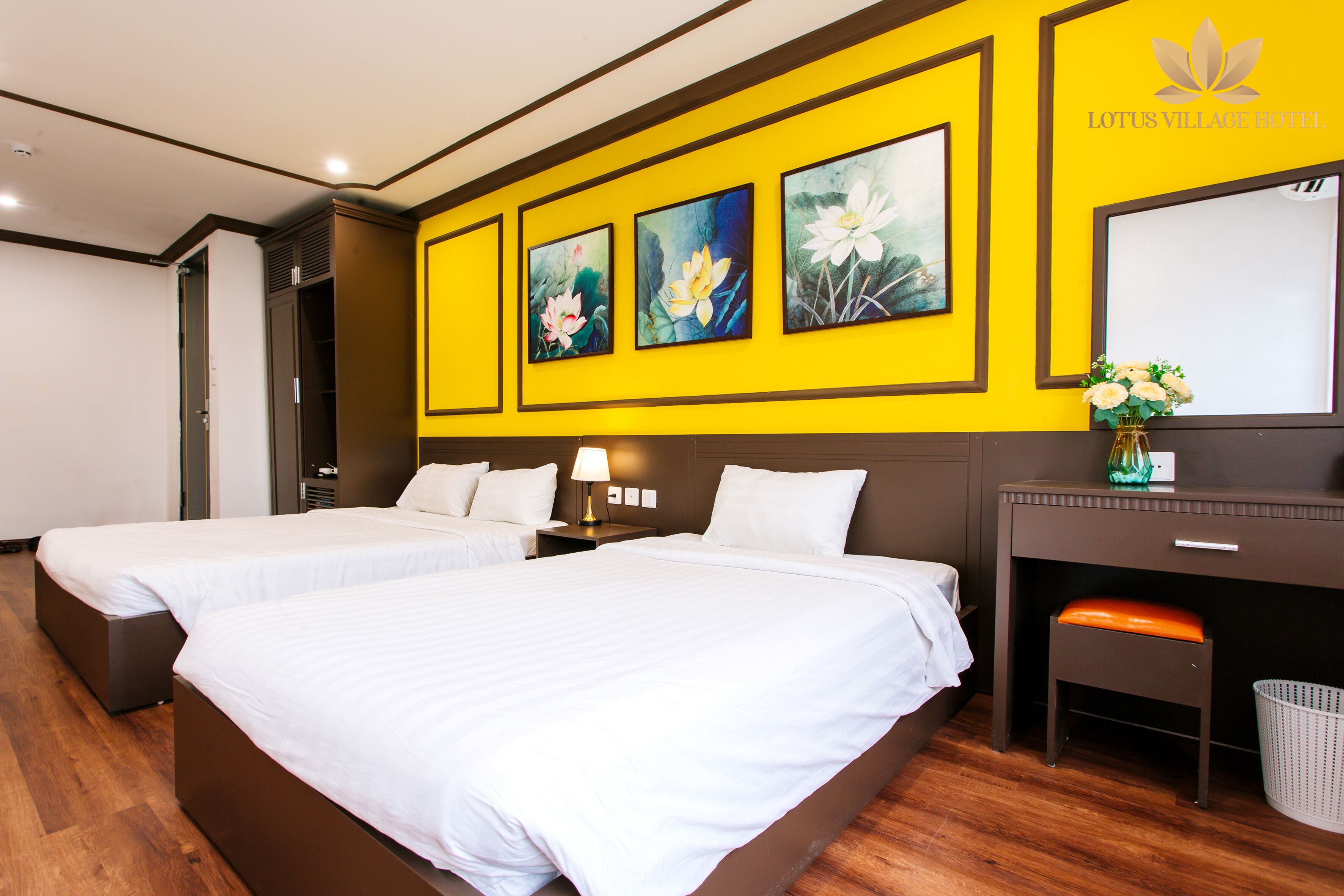 A hotel room with two beds, a desk, a chair, a lamp, and artwork on the wall.