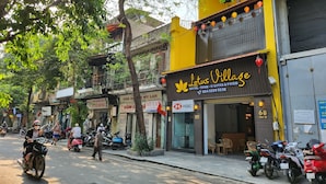 A street view with a hotel named Lotus Village, featuring a signboard with contact details and a logo. - Lotus Village Hotel (Hanoi)