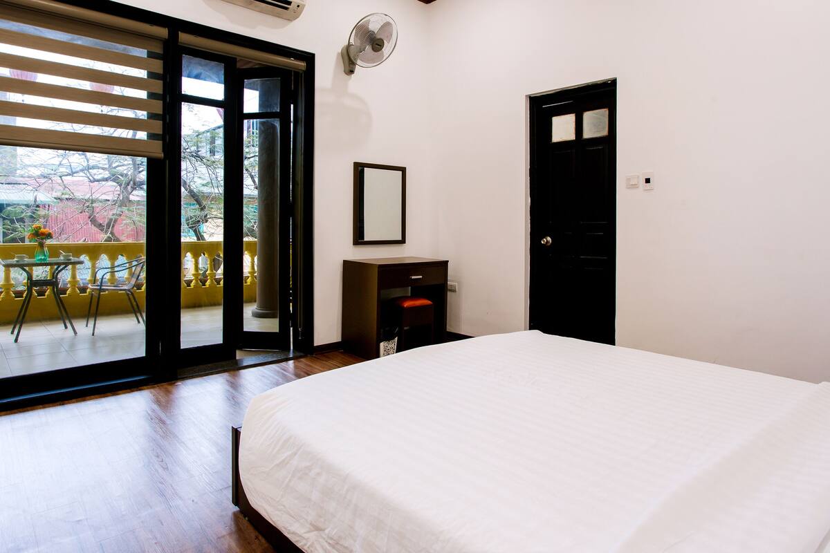 A bedroom with a bed, a desk with a chair, a window with blinds, and a door.