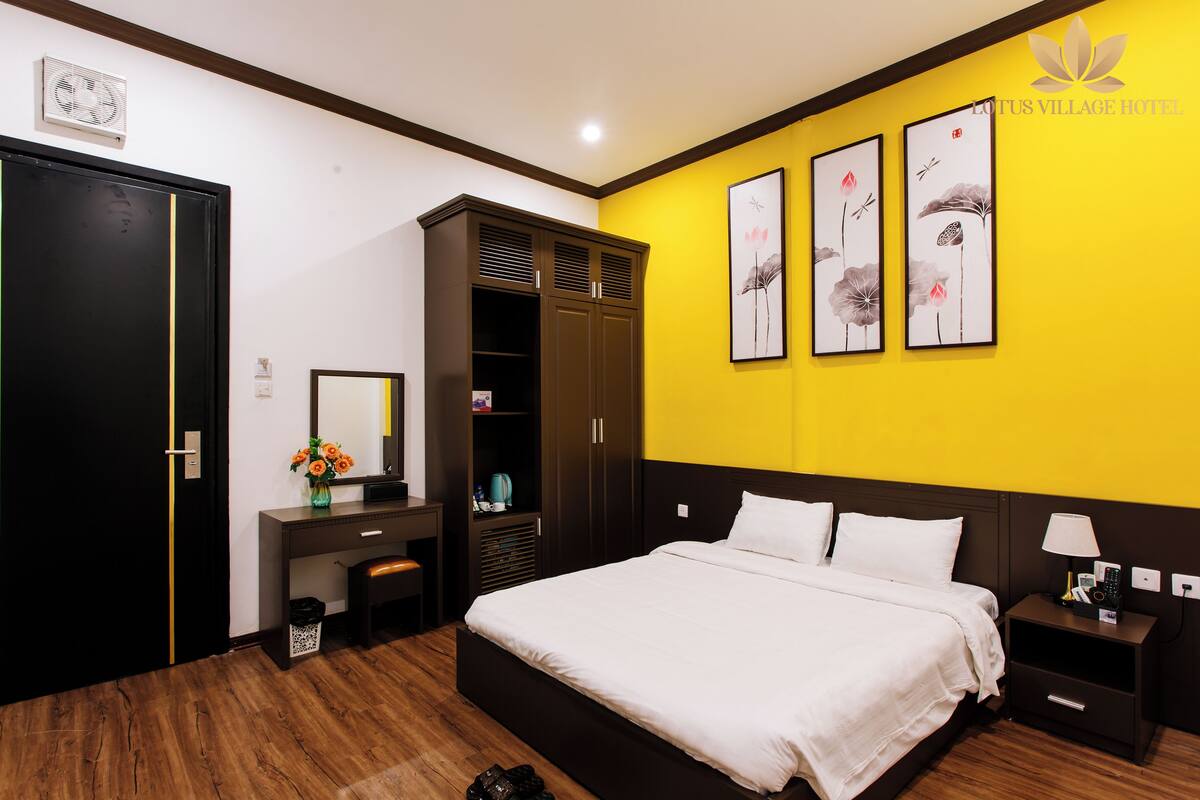 A hotel room with a bed, a desk, a wardrobe, and artwork on the wall.