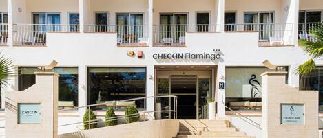 Entrada de un hotel con una escalera que lleva a la puerta, un cartel que indica Checkin Flamingo hotel y un letrero de bar lounge.