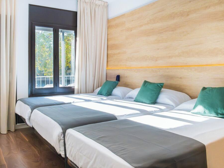 Habitación de hotel con dos camas, cabecero de madera y un ventanal con cortinas.