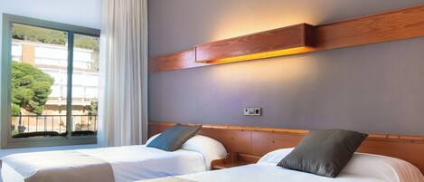 Een hotelkamer met twee bedden, een groot raam met gordijnen en een wandlamp.